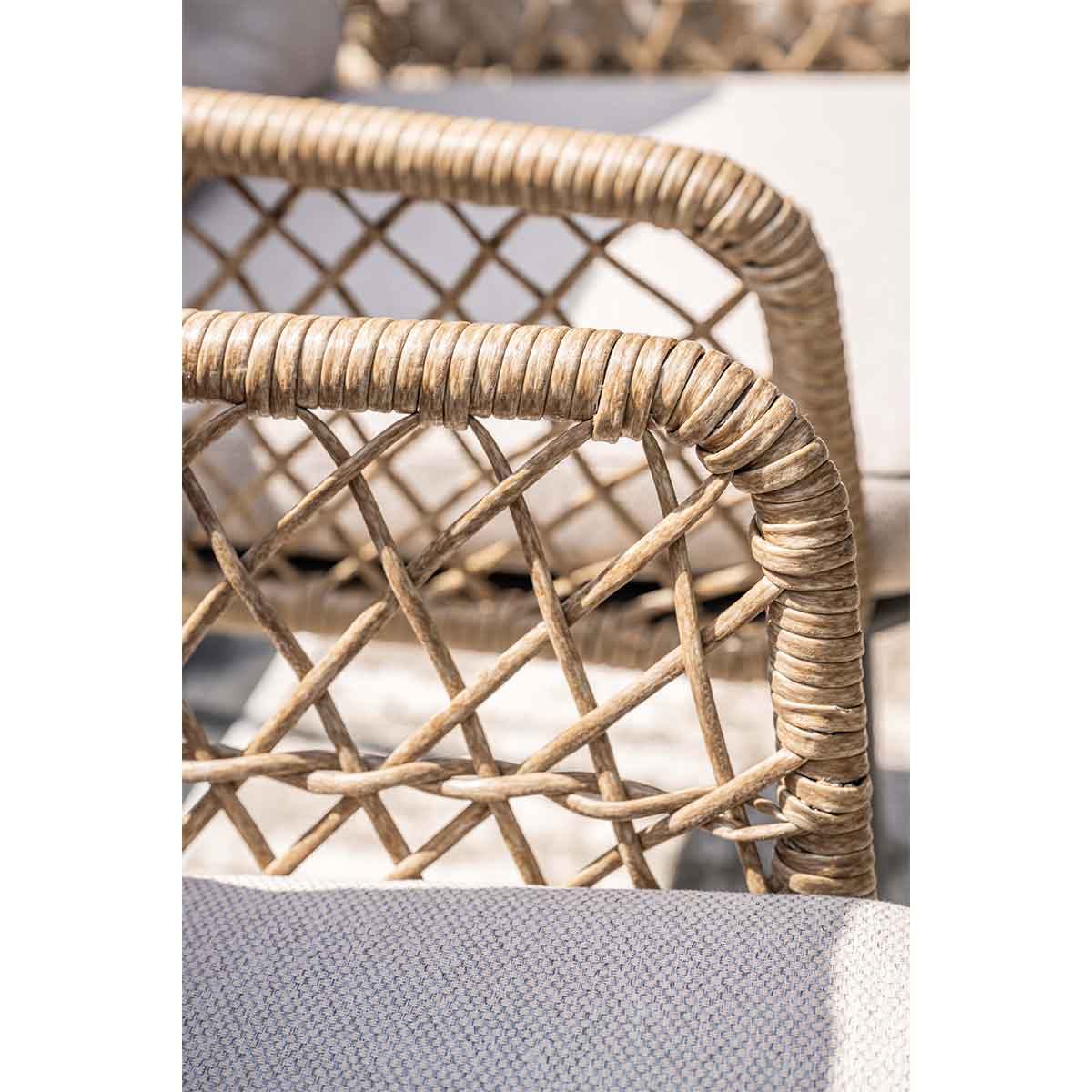 Close-up of a wicker chair arm.  Woven design in brown, with a gray cushion visible beneath.