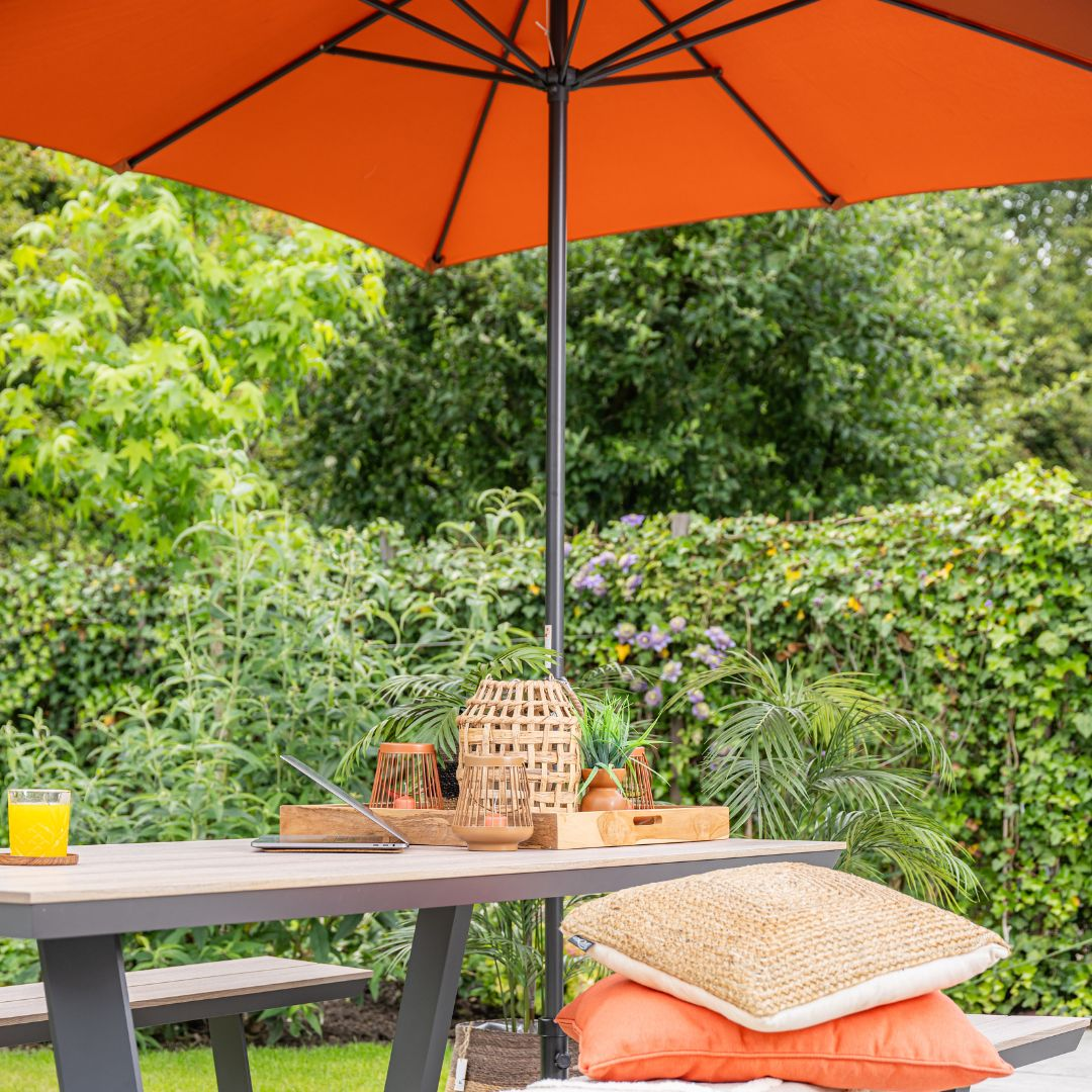 Outdoor dining table with orange umbrella, and decorative items. Green background.