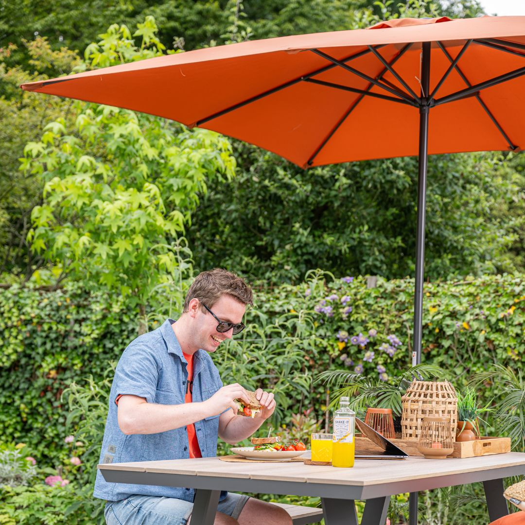 Man eating at a table under an orange umbrella.