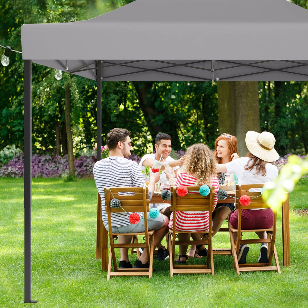 People seated at a table under a gray gazebo in a garden, enjoying a meal.