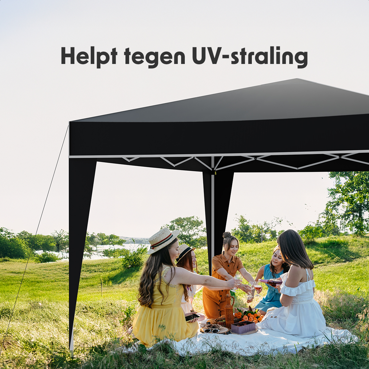 Four women under a black tent. They are enjoying drinks. A picnic basket is on the mat.