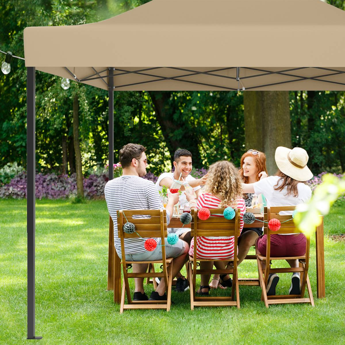 People dining under a tan tent in a garden, with wooden chairs and a string of lights.