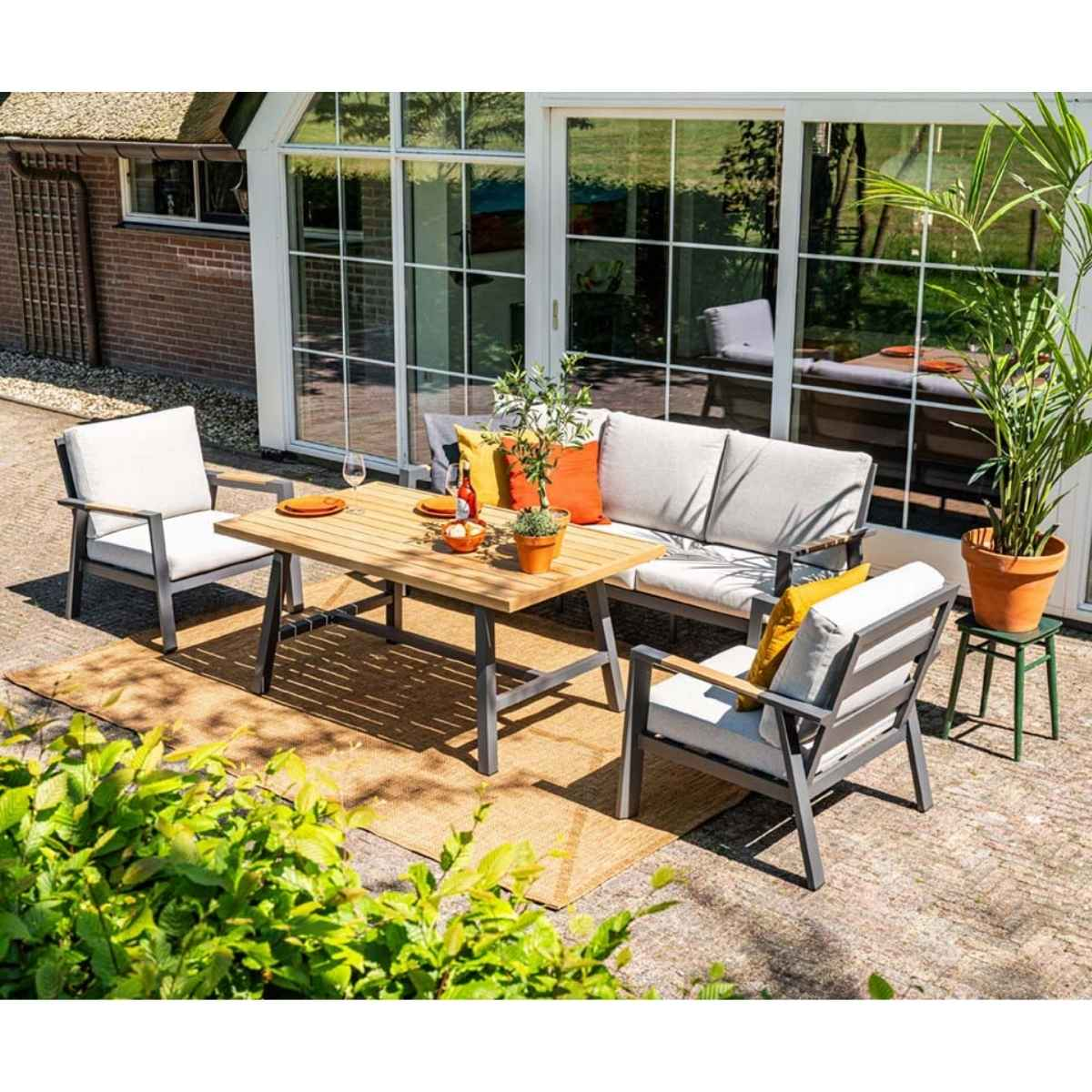 Tuinset: tafel, bank en stoelen op een vloerkleed, planten in potten en glazen deuren.