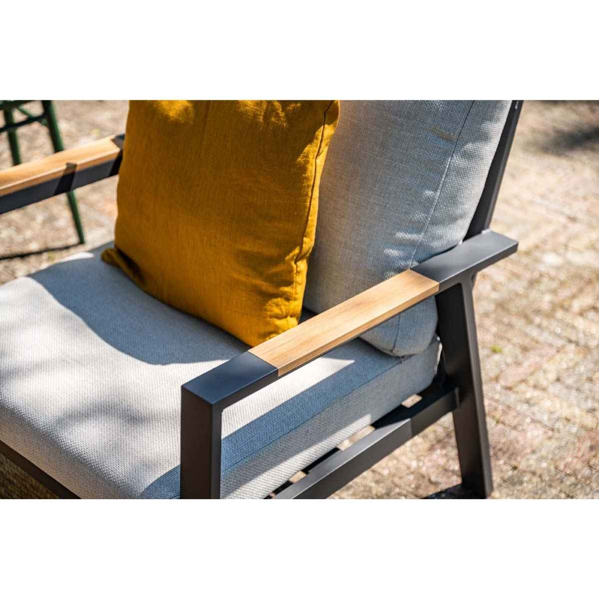 Buitenstoel met houten armleuningen en geel kussen; op een bakstenen terras.
