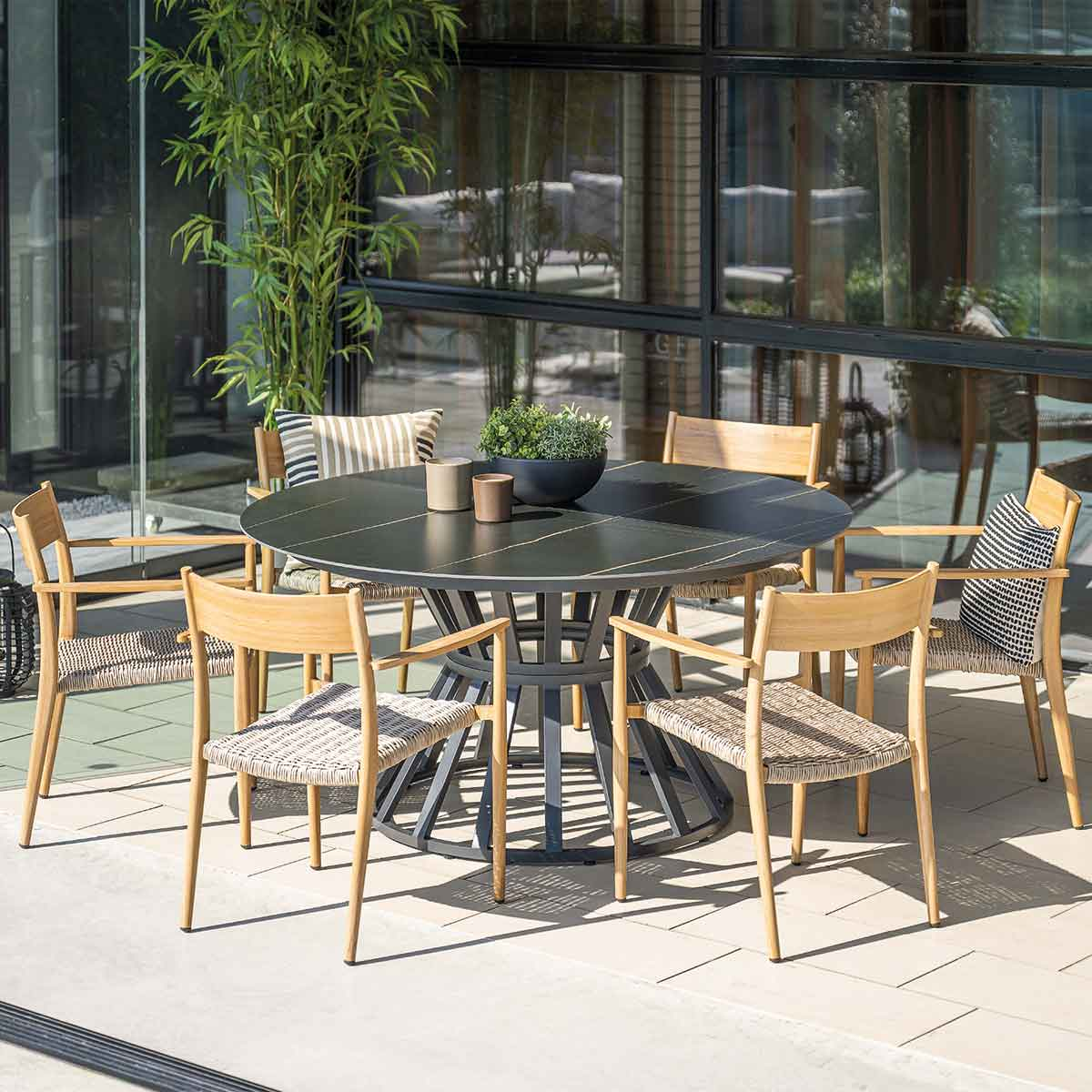 Ronde zwarte tafel met zes stoelen. Tafel in het midden, stoelen eromheen. Groene achtergrond.