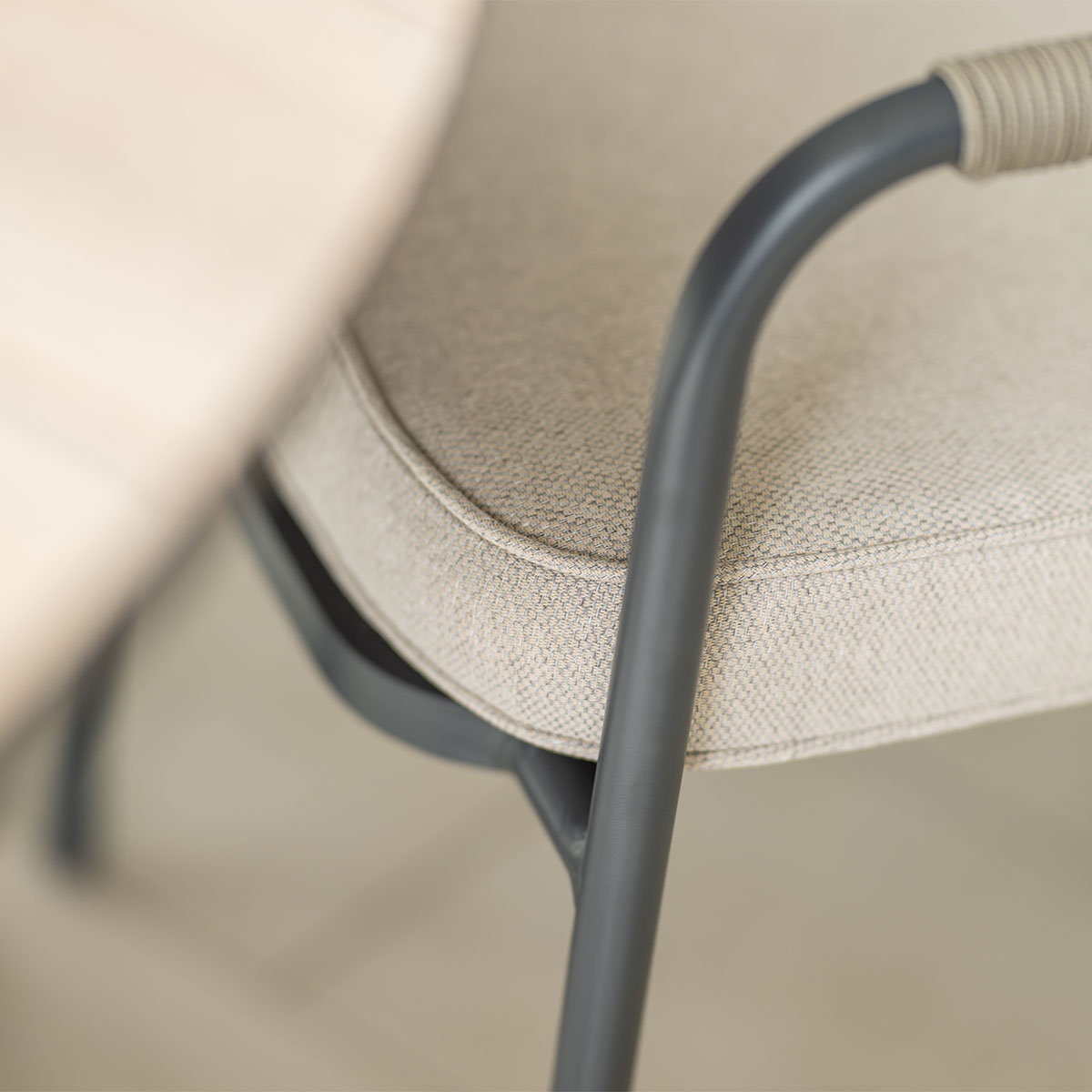 Close-up of a beige chair with a gray frame. The chair is near a light-colored wooden table.