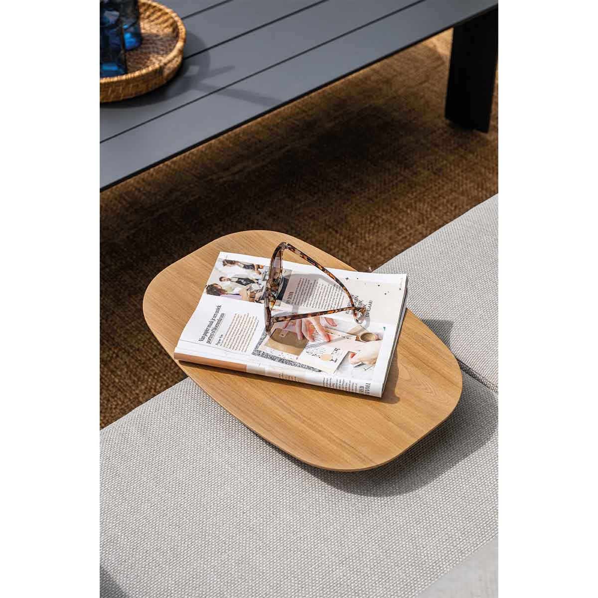 Gros plan d'un plateau en bois avec des lunettes de soleil et un magazine dessus, placé sur un canapé.