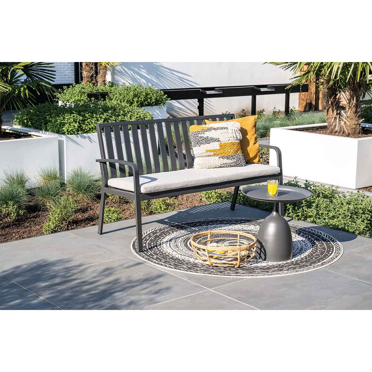 Un banc, une petite table avec une boisson et un tapis sur un patio.