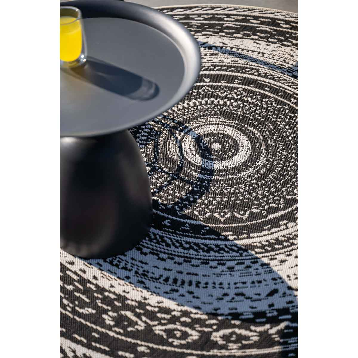 Une table noire avec une boisson et un tapis avec un motif circulaire.