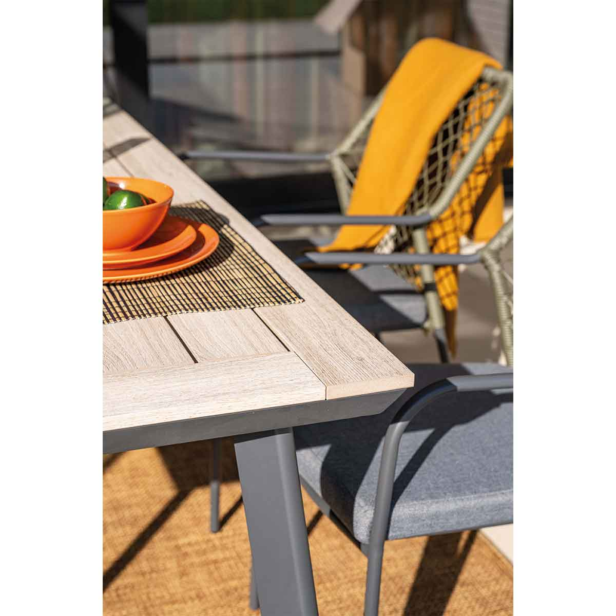 Close-up of a table setting with a placemat, orange plates, and a bowl. A chair with a yellow blanket is behind.