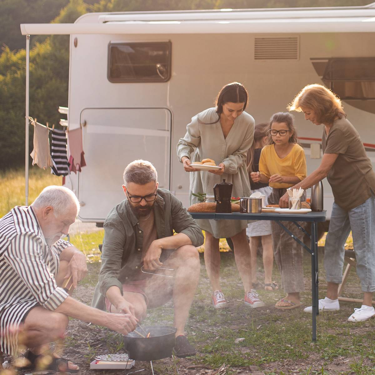 Familie rond een campingtafel naast een camper.
