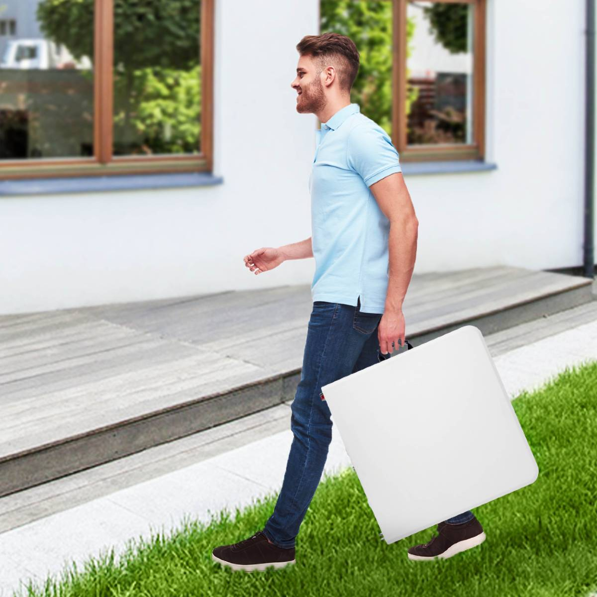 Man die een witte opvouwbare tafel draagt, lopend op een pad. Groen gras aan de zijkant.