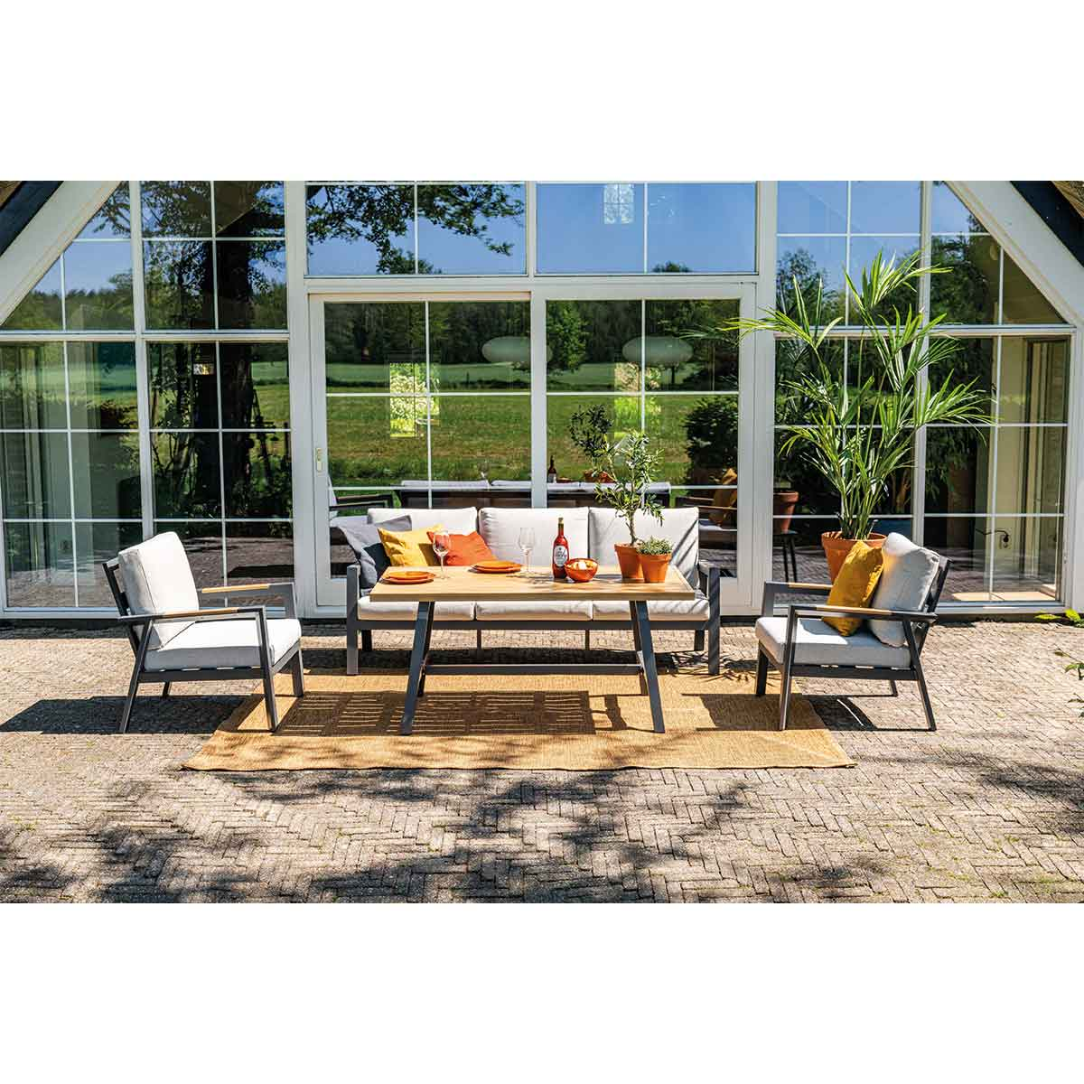 Terras met tafel, stoelen, bank en planten. Witte muren, glazen ramen.