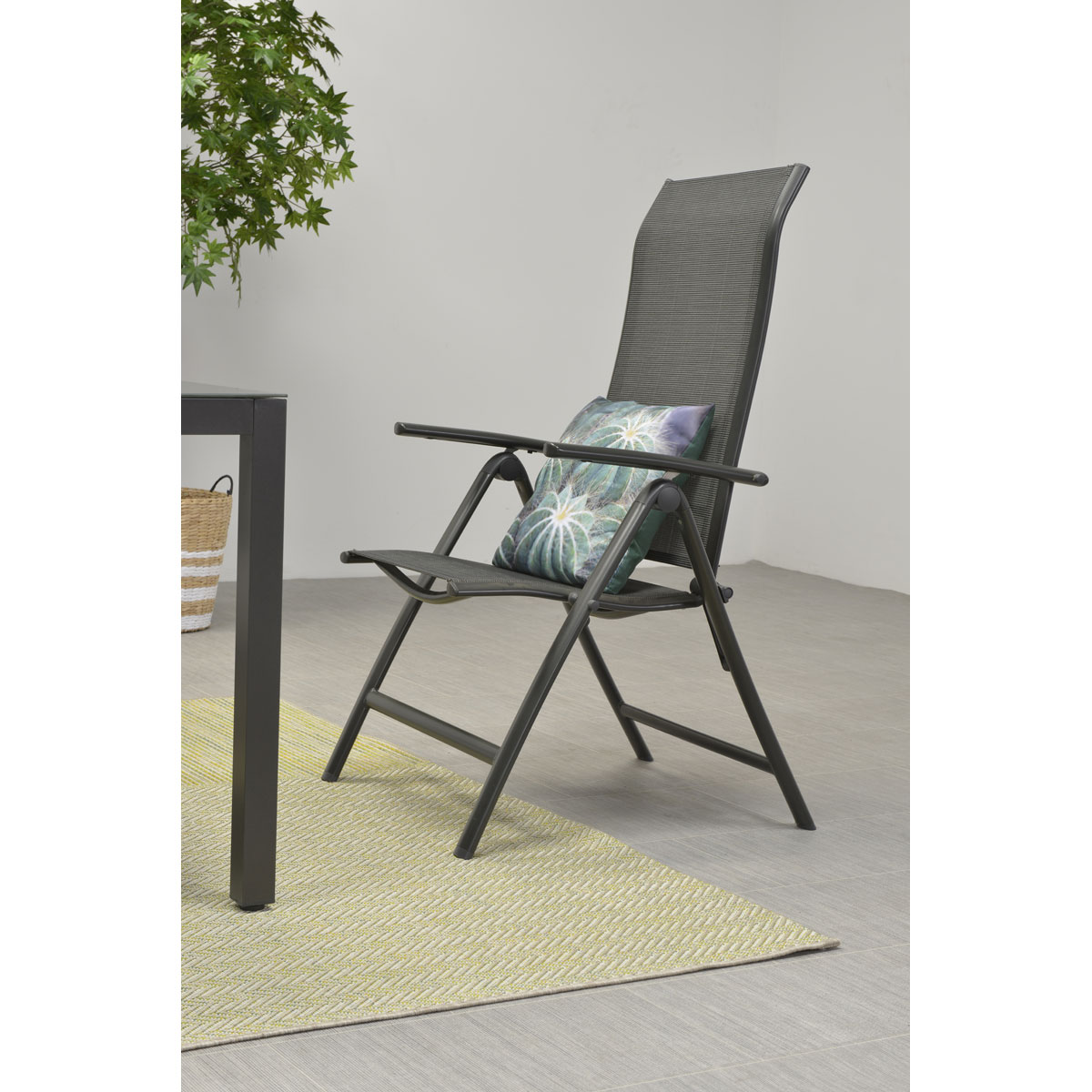 Outdoor folding chair with gray fabric and a decorative pillow, next to a table.