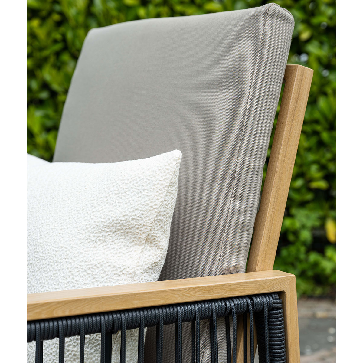 Close-up van tuinmeubelen: grijs kussen, wit kussen, zwart touwdetail, houten frame.