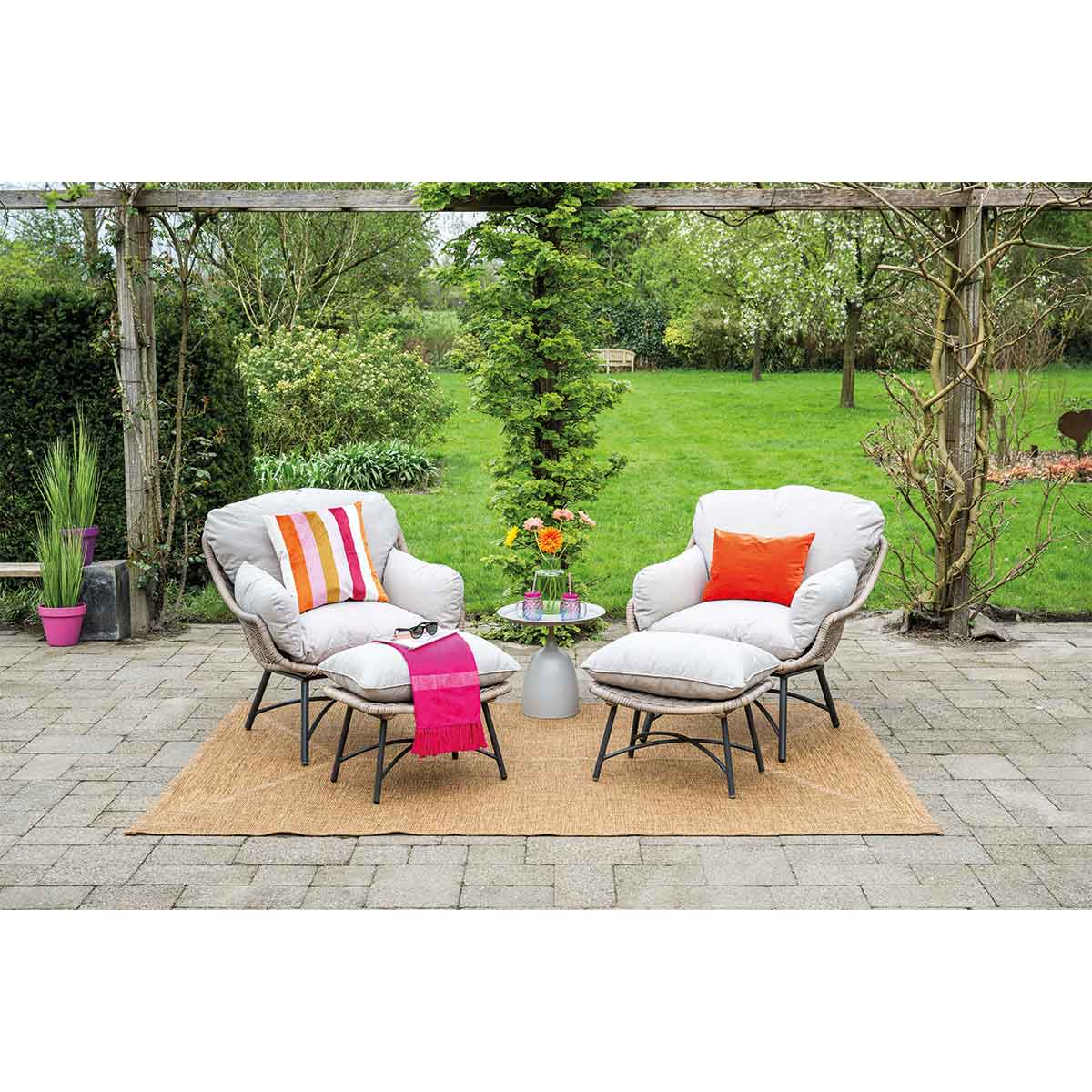 Outdoor patio set with two chairs, ottomans, table, and colorful pillows on a rug.