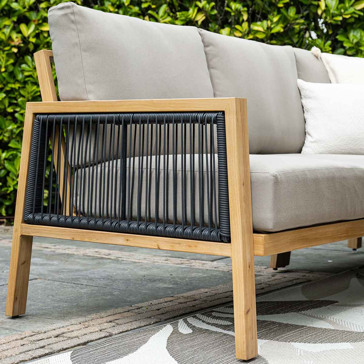 Buitensofa met houten frame, zwarte touwdetails en lichtgrijze kussens. Witte achtergrond.