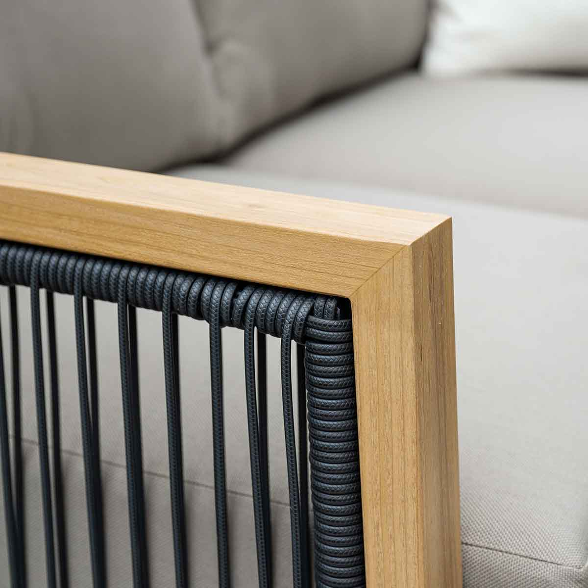 Close-up van een houten framehoek met zwart touw, grijs kussen en bank.
