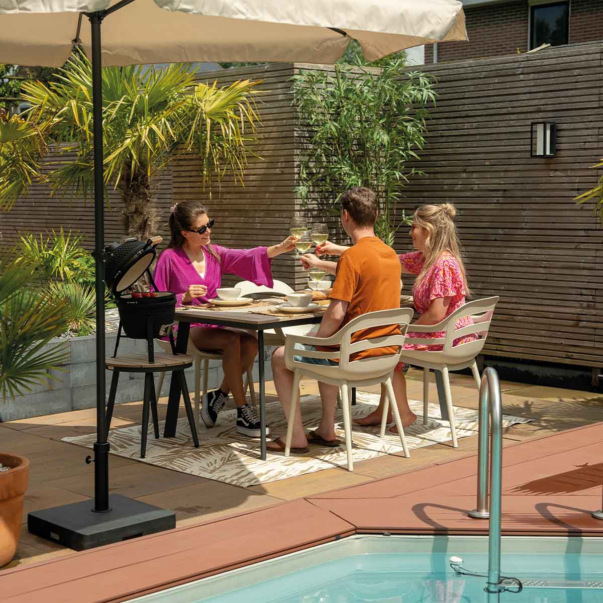 Group of people toasting drinks at an outdoor table, under a parasol. Bright sunny scene.