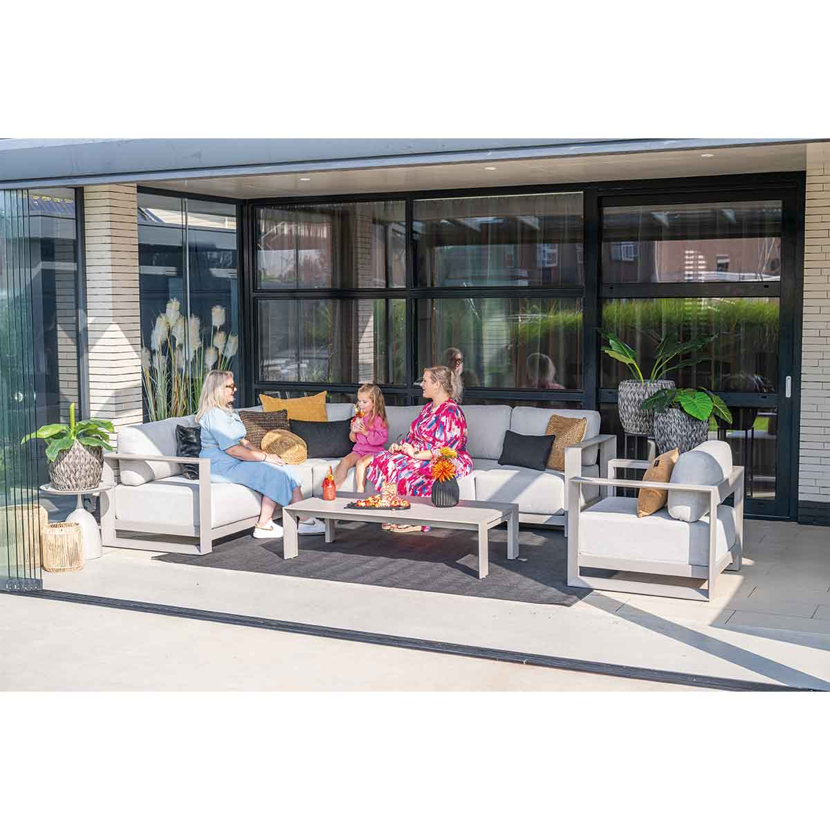 Buitenscène met mensen. Bank, tafel, stoelen, tapijt. Mensen zitten en praten.