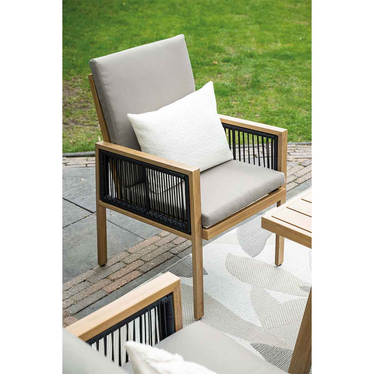 Outdoor chair with cushions. Black rope accents. Set on a patio with a grass background.