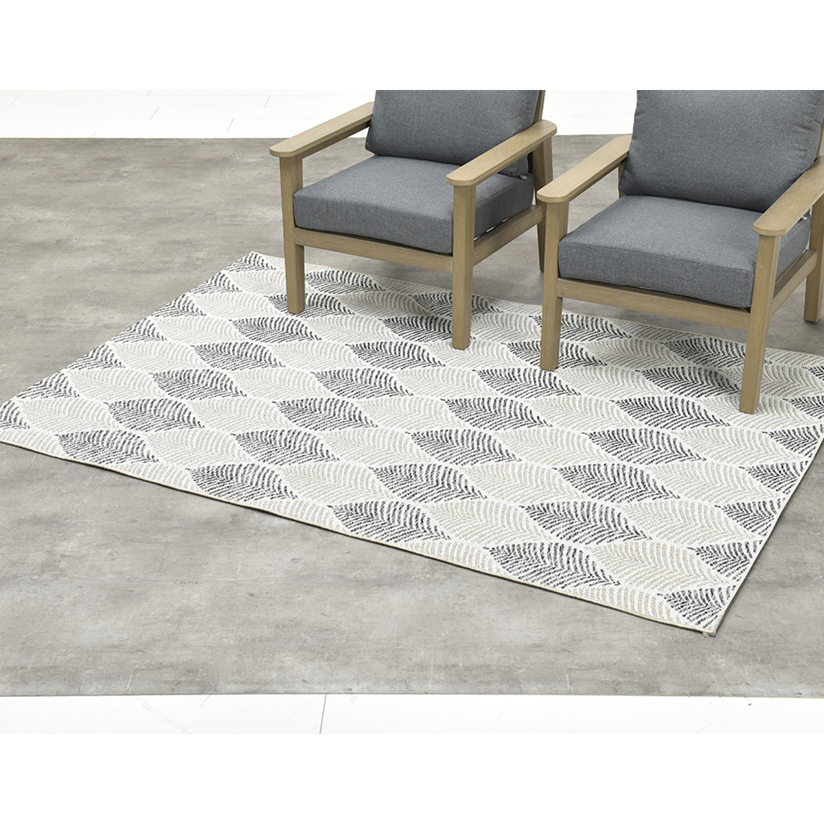 Twee stoelen op een kleed met bladerpatroon, geplaatst op een betonnen vloer.