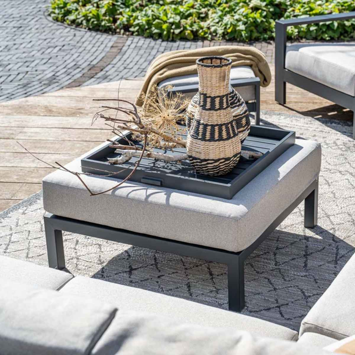 Outdoor seating area with a gray ottoman and a decorative vase on a tray.