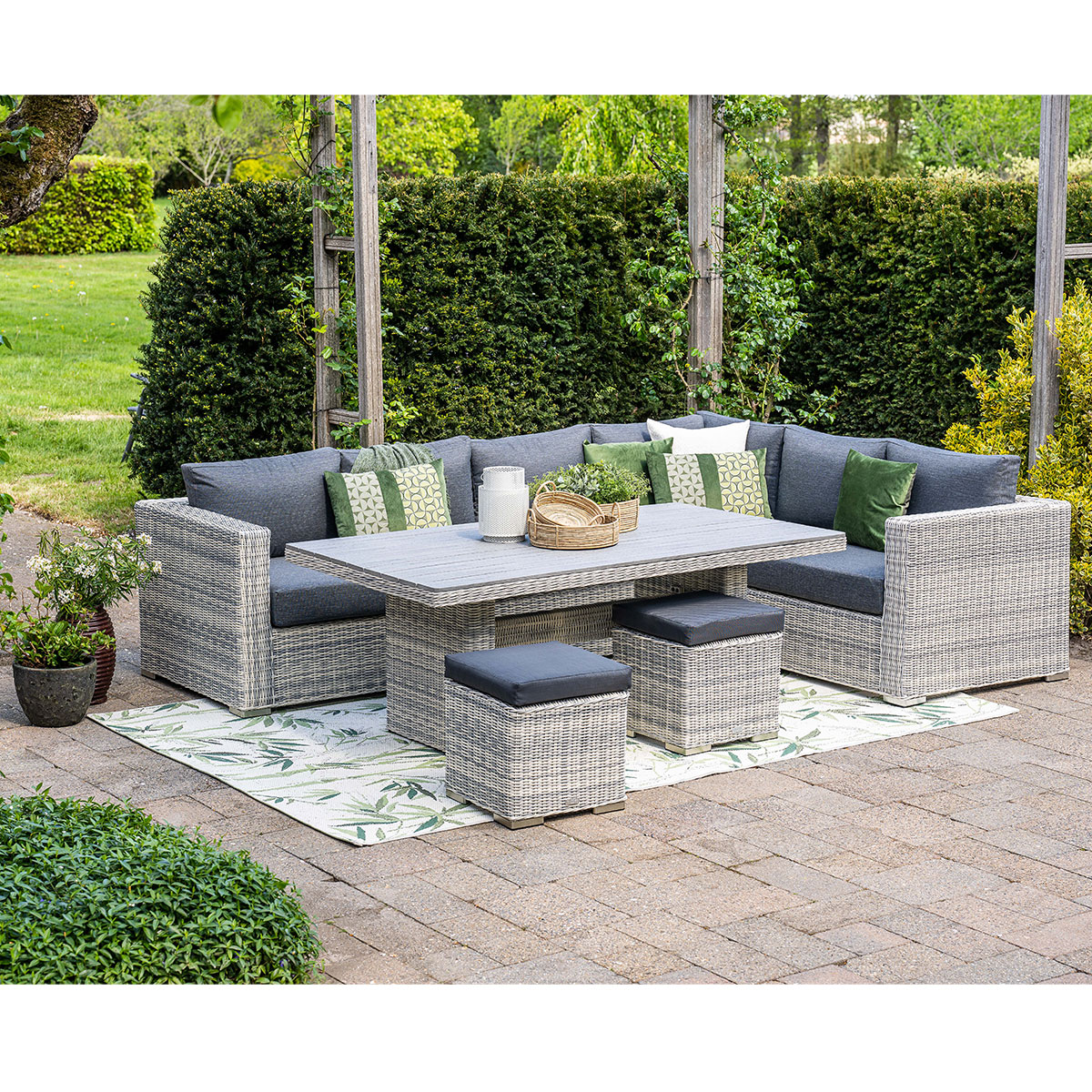 Ensemble sectionnel extérieur en osier gris avec table et tabourets, sur un tapis à motifs verts.