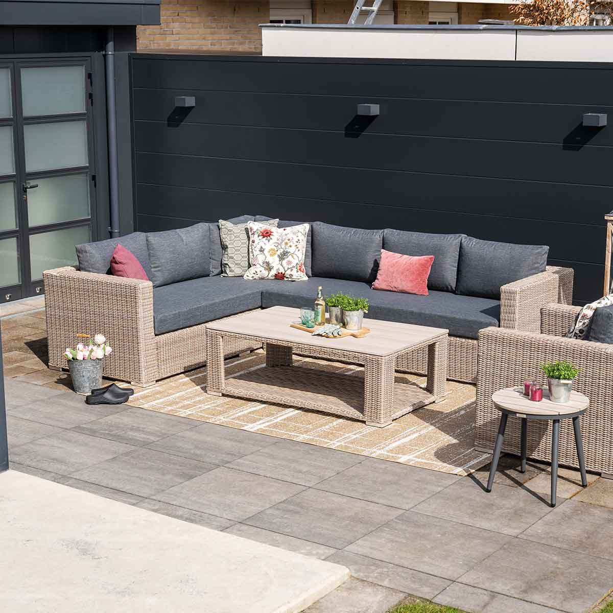 Espace extérieur avec canapé sectionnel, table, tapis, plantes, accessoires et un fond sombre.