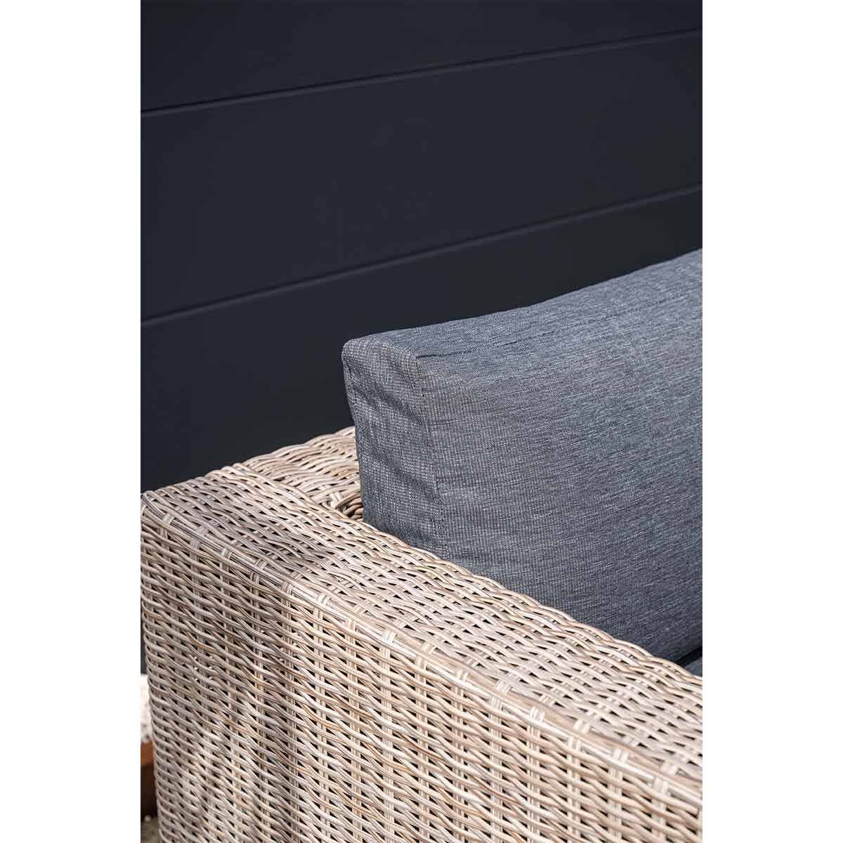 Gros plan d'une chaise en osier avec un coussin gris et un mur sombre.