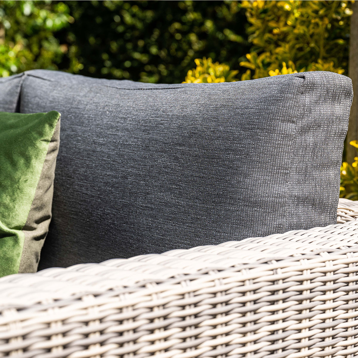 Gros plan d'un coussin gris sur une chaise en osier avec un oreiller vert.