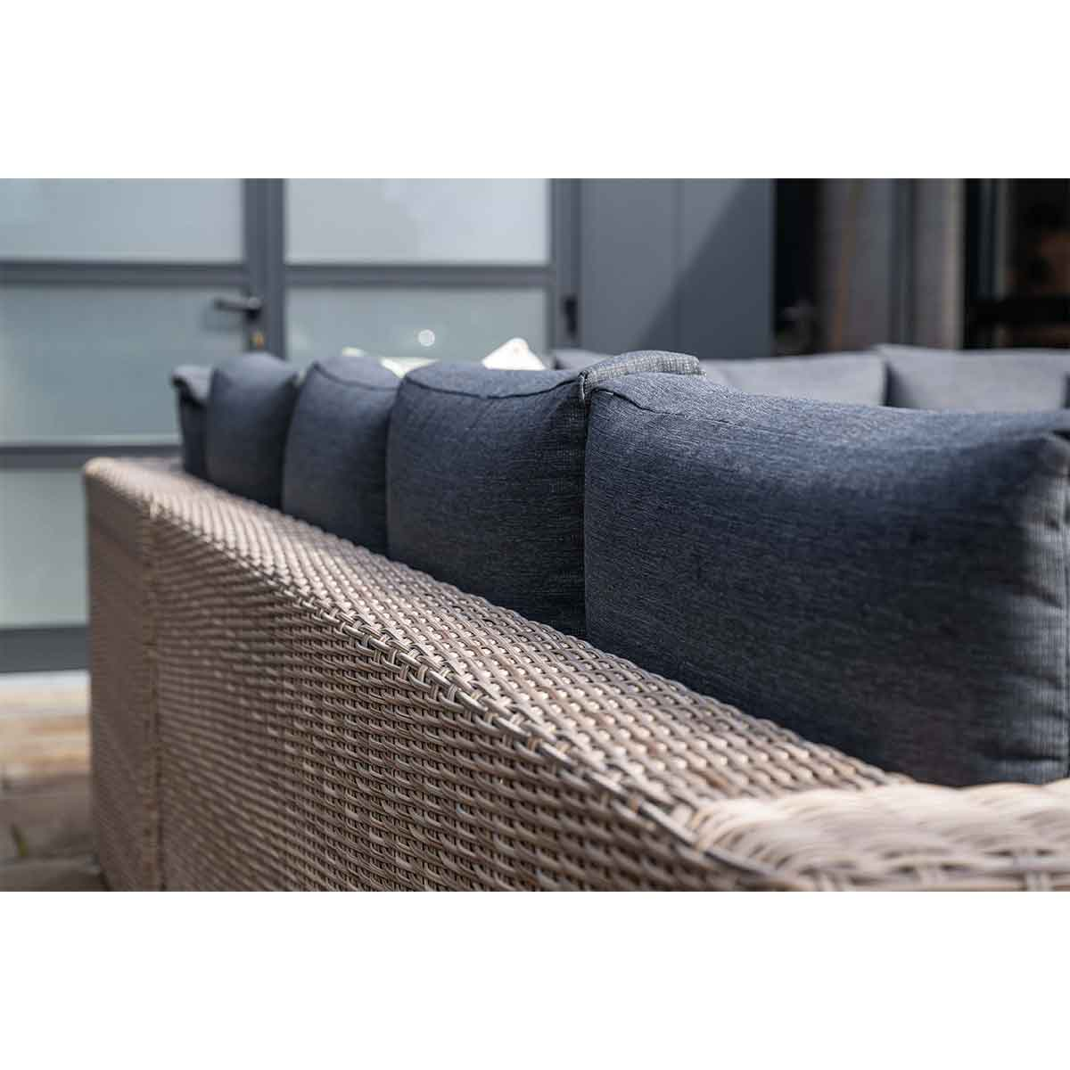 Gros plan d'un canapé extérieur tissé, montrant les coussins gris et le cadre tissé.