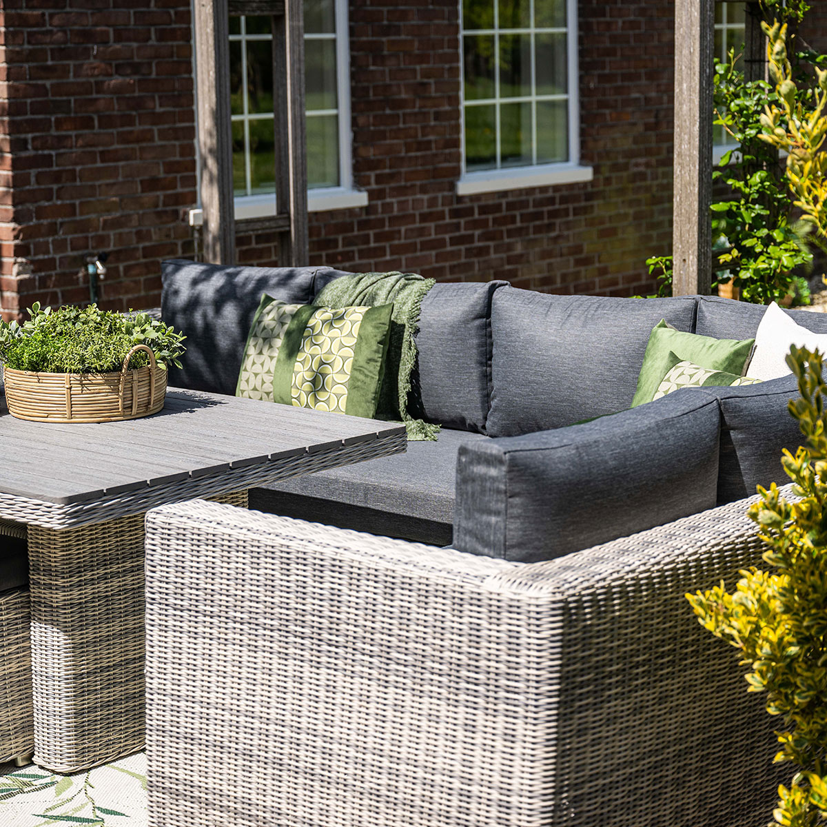 Ensemble de patio extérieur avec coussins gris, table et meubles en osier. Mur en briques.