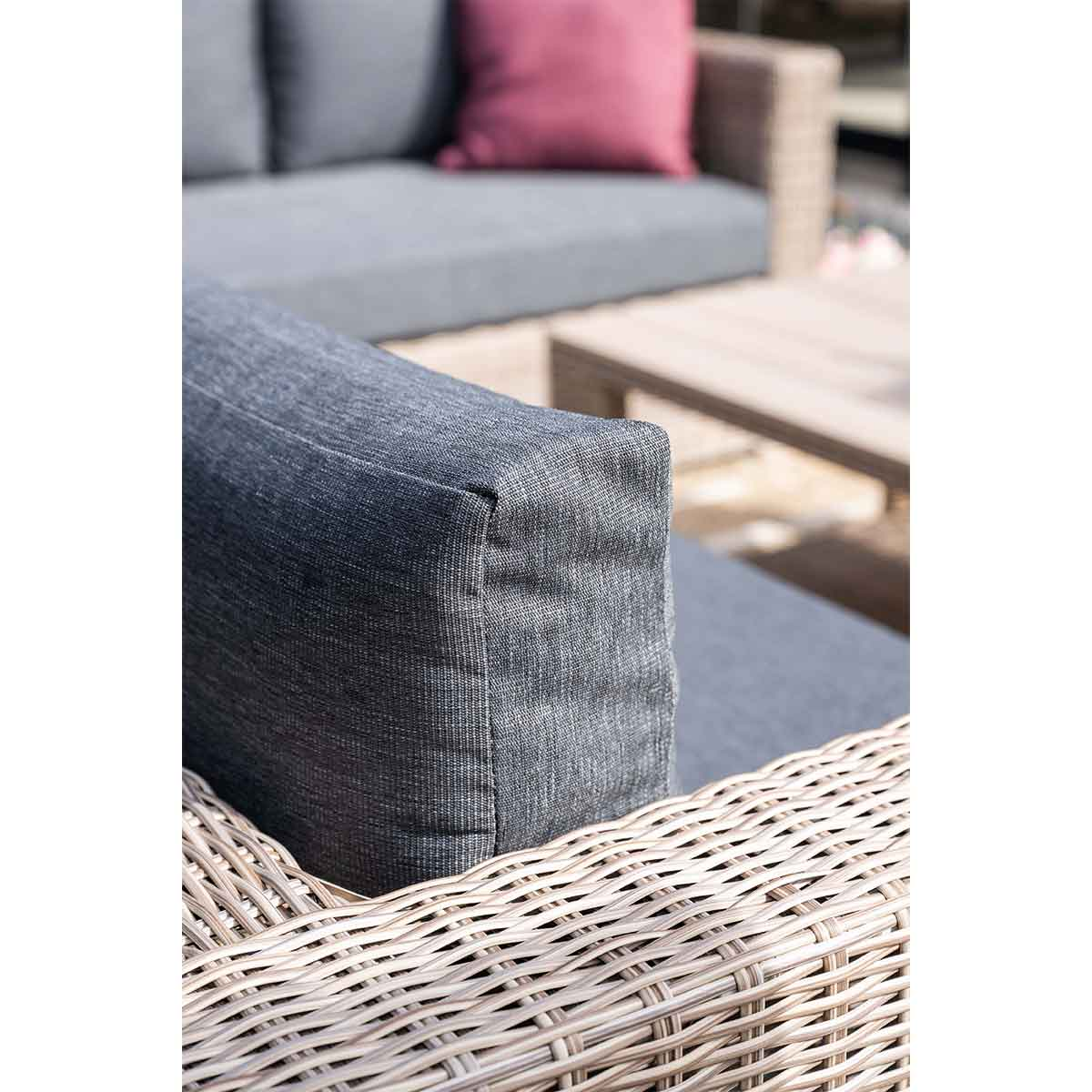 Gros plan : détail du coin d'un canapé extérieur, montrant coussin gris et cadre en osier.