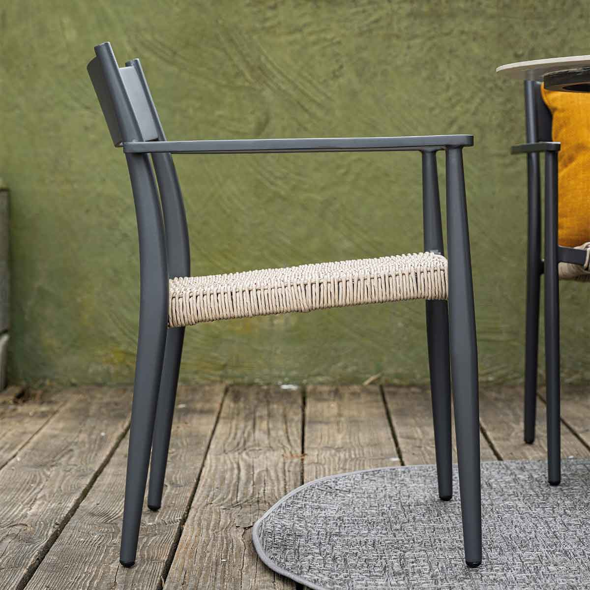 Zijaanzicht van een grijze stoel met geweven zitting. Op houten terras.