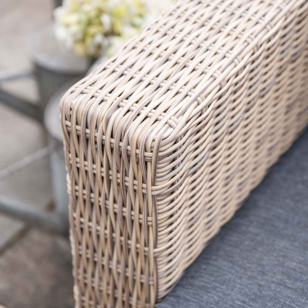 Gros plan sur l'accoudoir en osier tressé. Coussin gris visible en dessous.