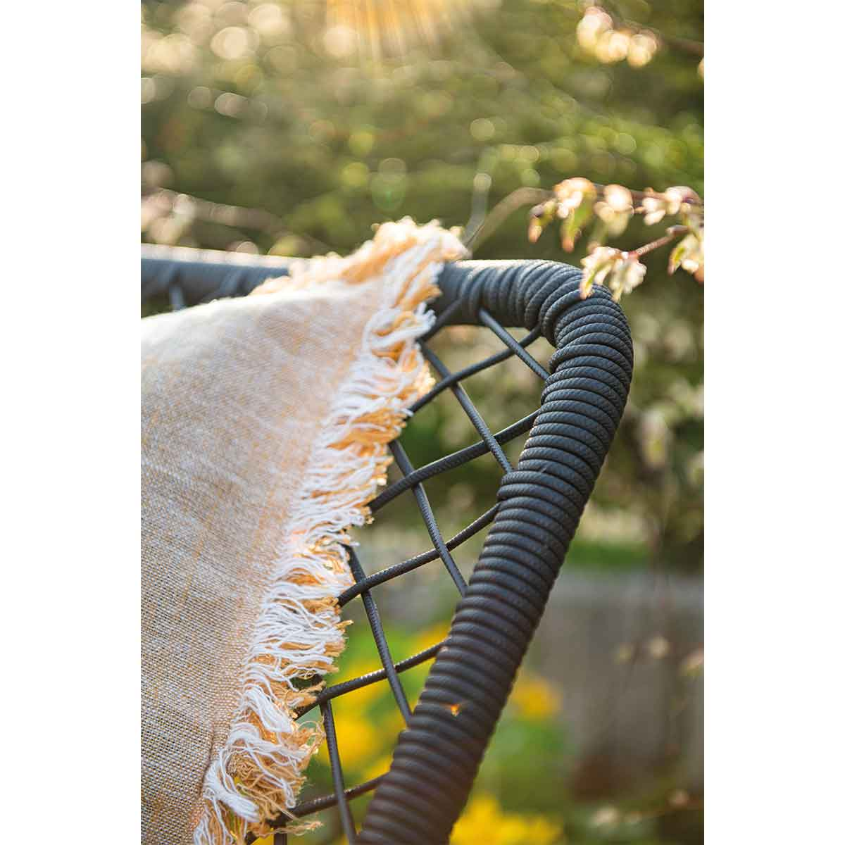 Close-up of woven chair back with a tan blanket draped over it. Blurred green background.