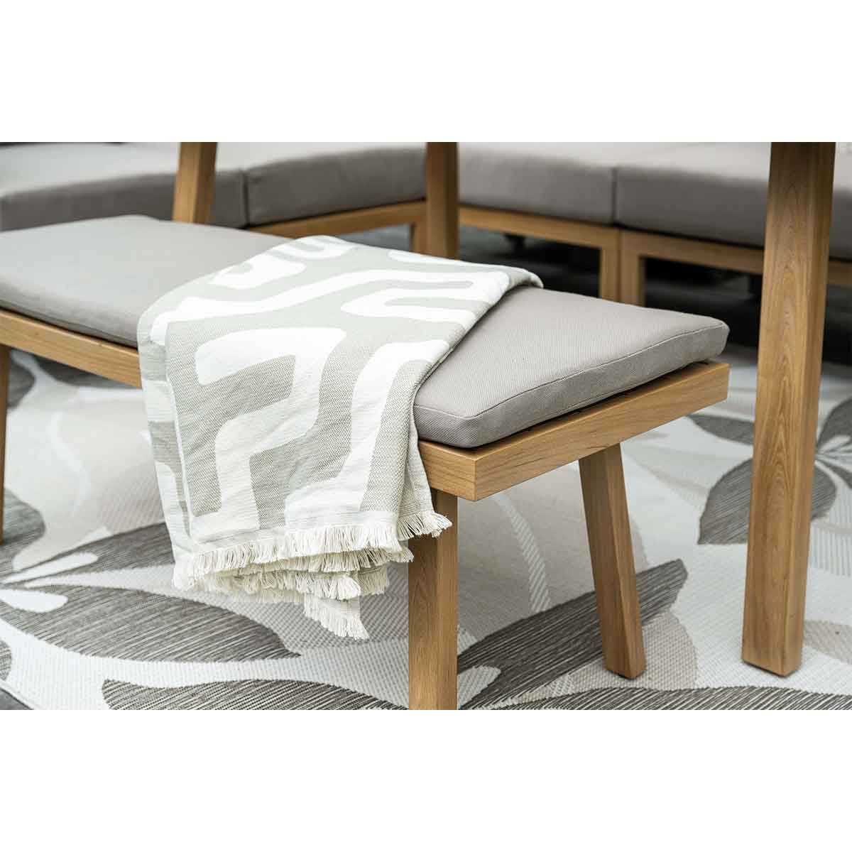 Bench with a blanket and pillows. The bench is on a patterned rug.