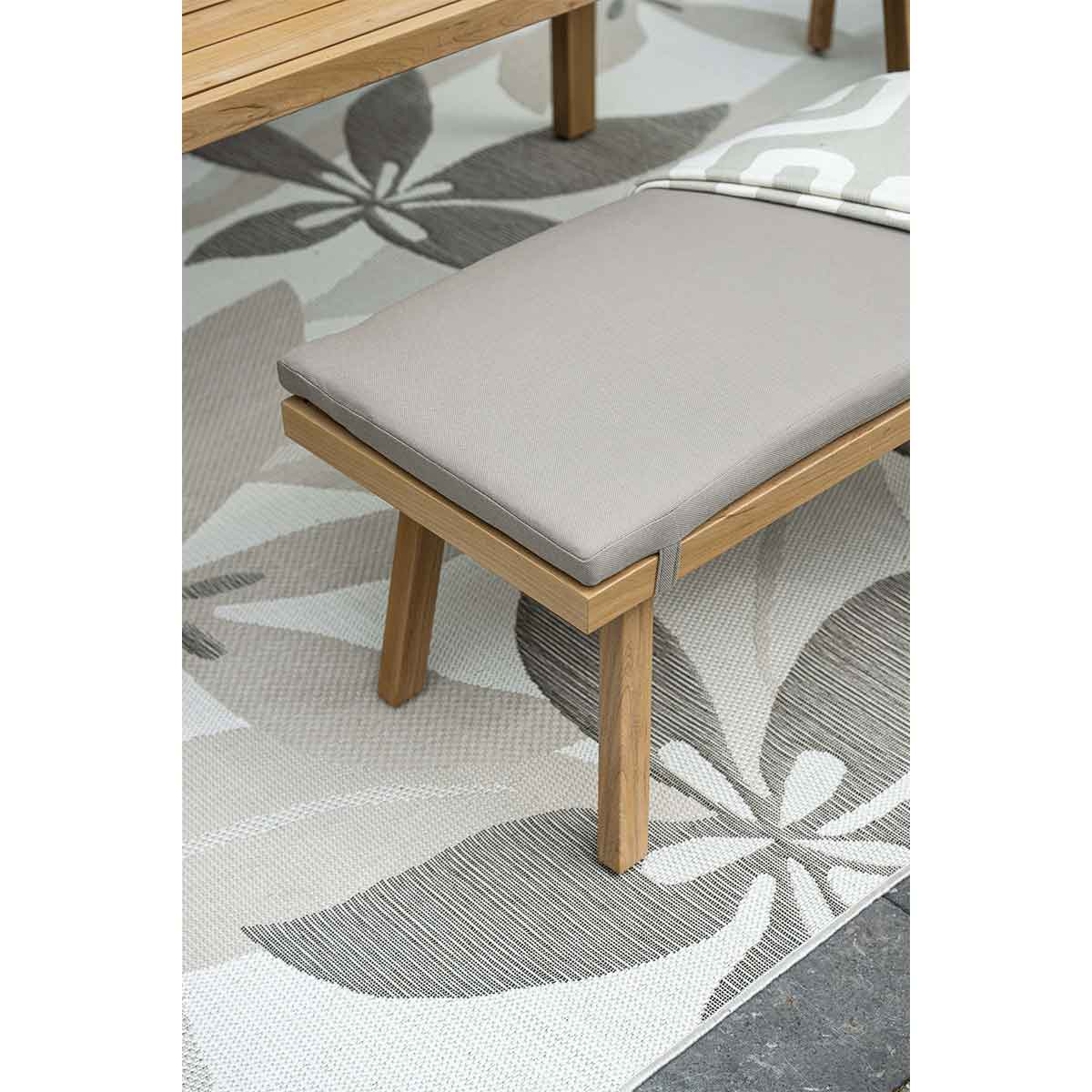 A wooden bench with gray cushion on a rug with large gray and white floral design.