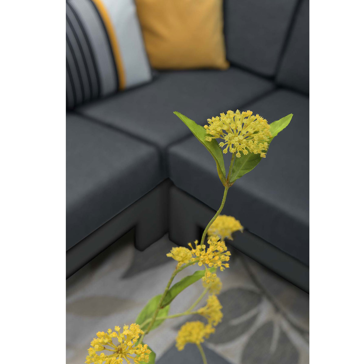 Yellow flowers with green leaves, set against a dark grey sofa.