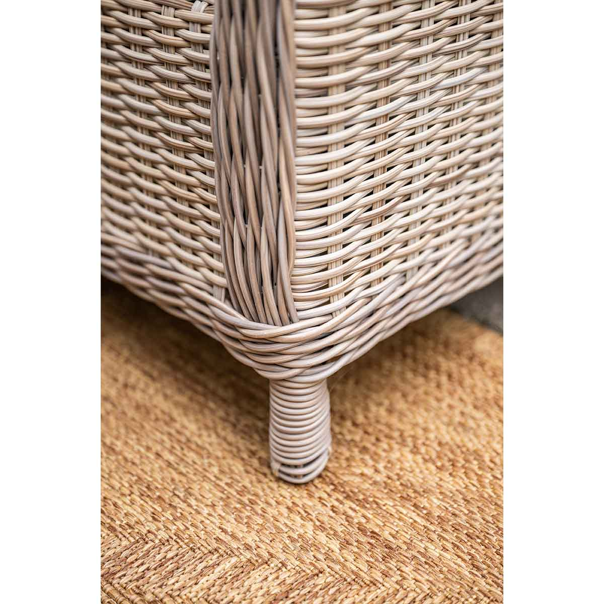Close-up of a woven gray, rattan-like leg of a chair or sofa, on a textured rug.