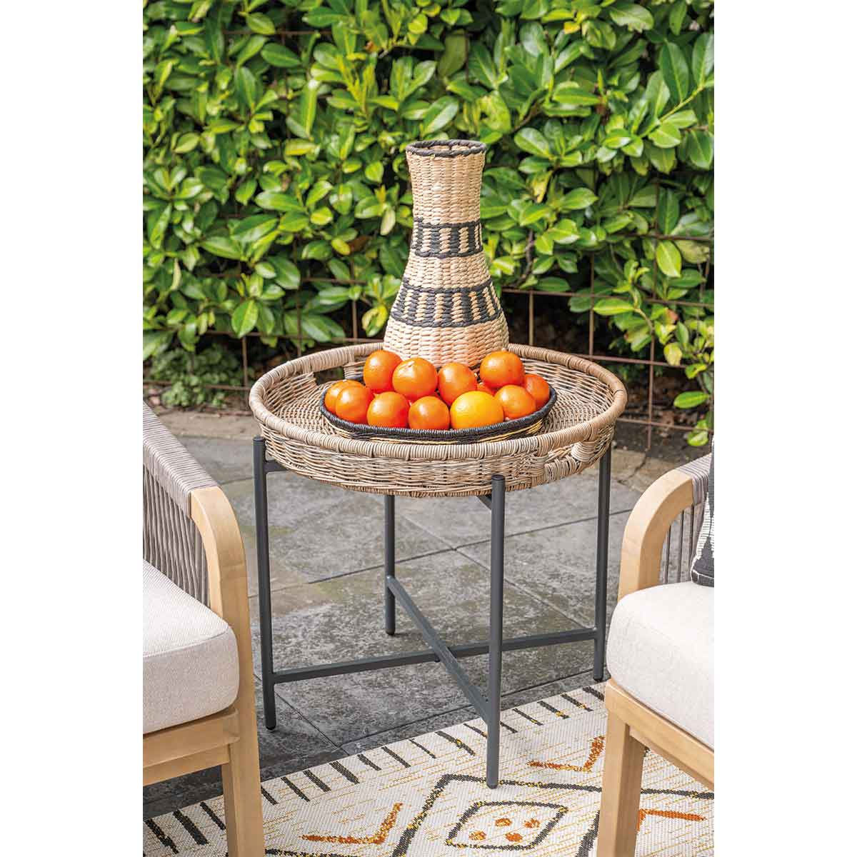 Table en plein air avec oranges, vase et chaises. Table en osier, fond de haie verte.