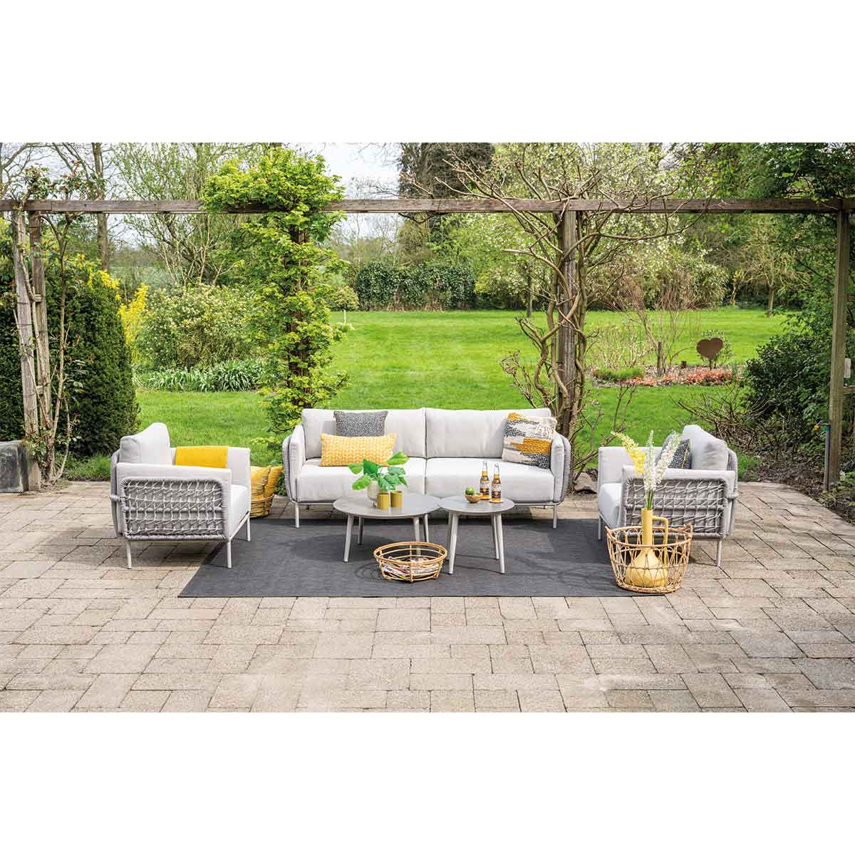 Outdoor patio with seating, small tables, and plants. Neutral colors, with a garden backdrop.