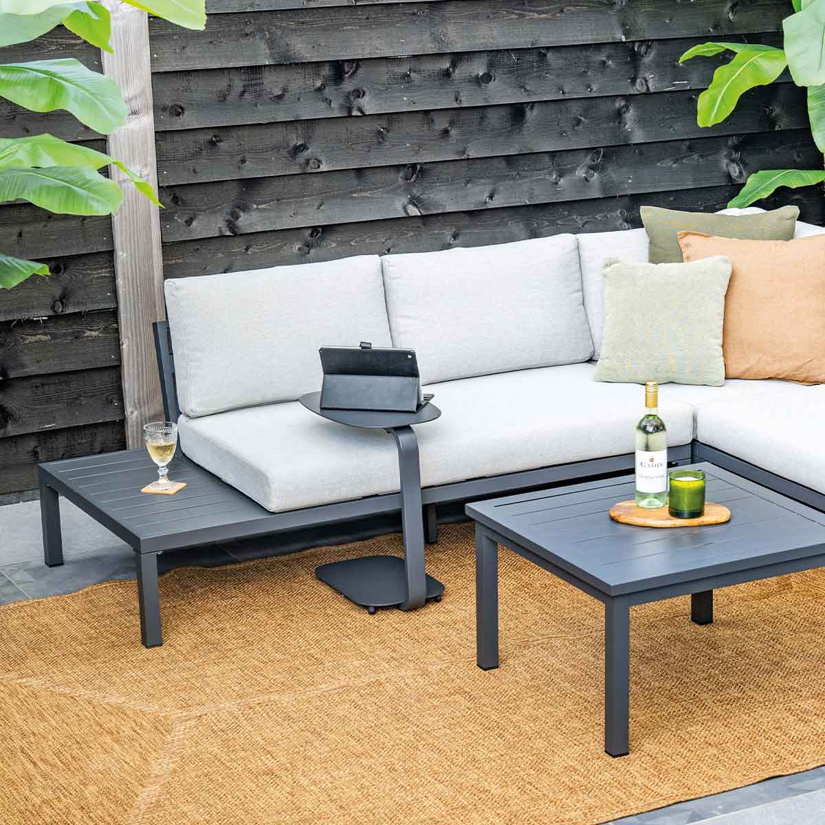 Coin salon extérieur avec mobilier gris, tapis et une table d'appoint.