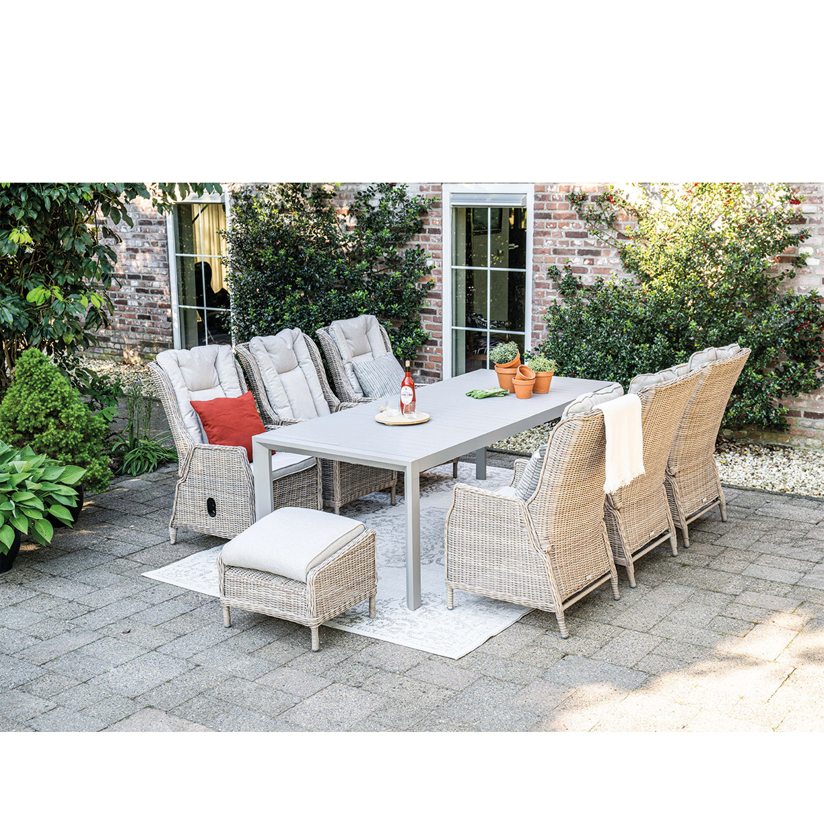 Buiteneetset met stoelen, tafel, kussens en planten op een terras.