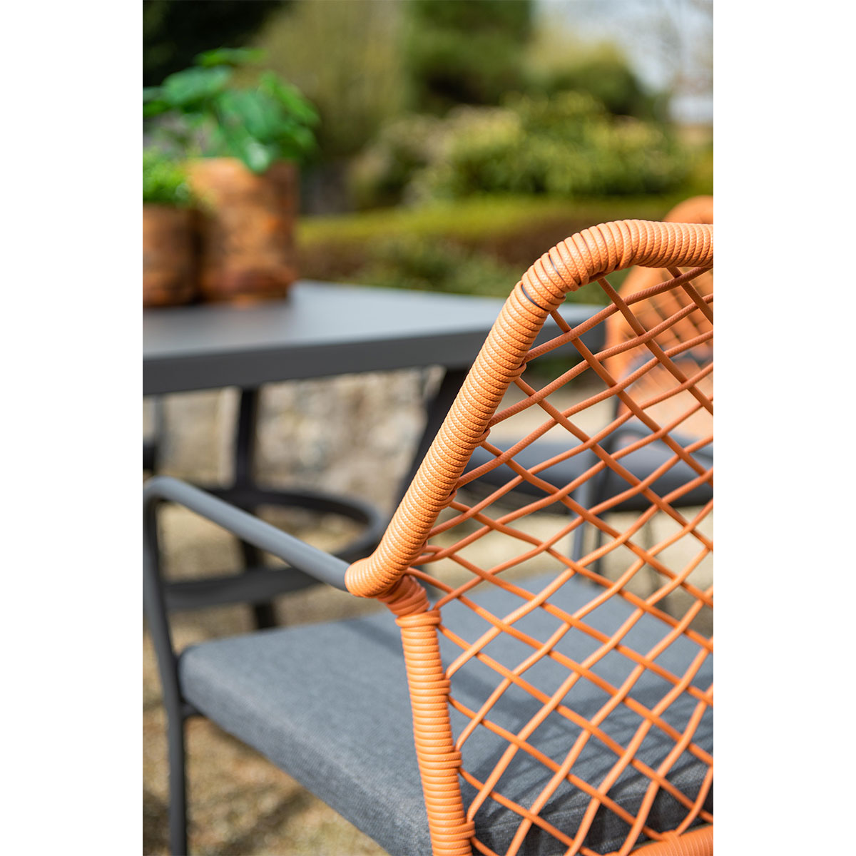 Close-up of an orange woven chair, gray cushion, and a table, with blurred background.