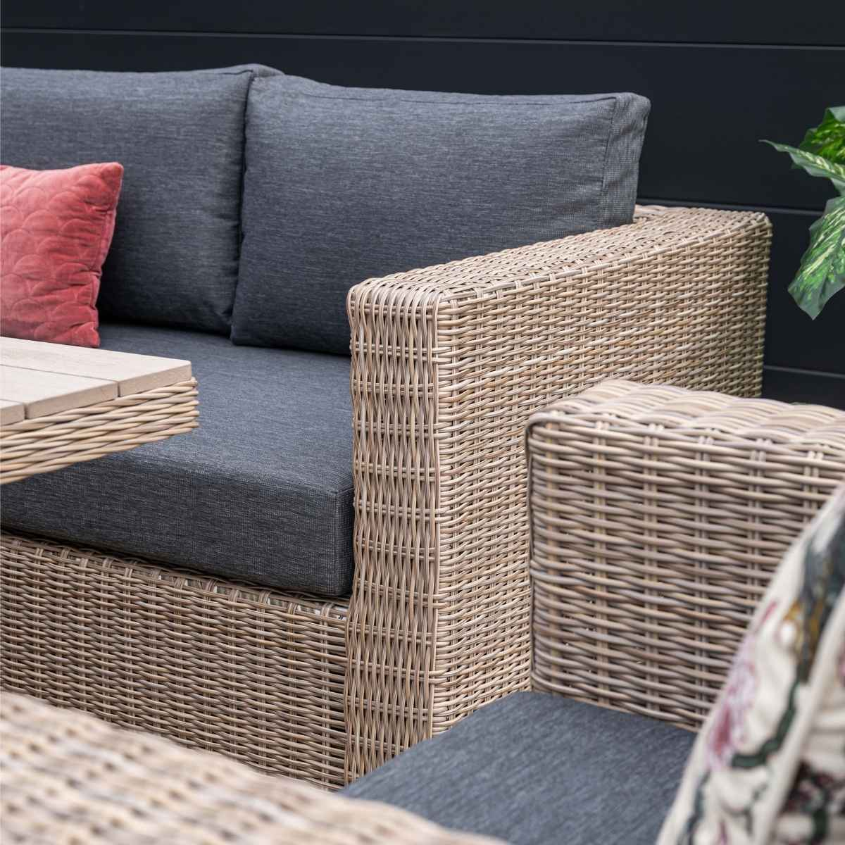Coin de canapé en osier avec coussins gris et coussin rouge. Fond sombre.