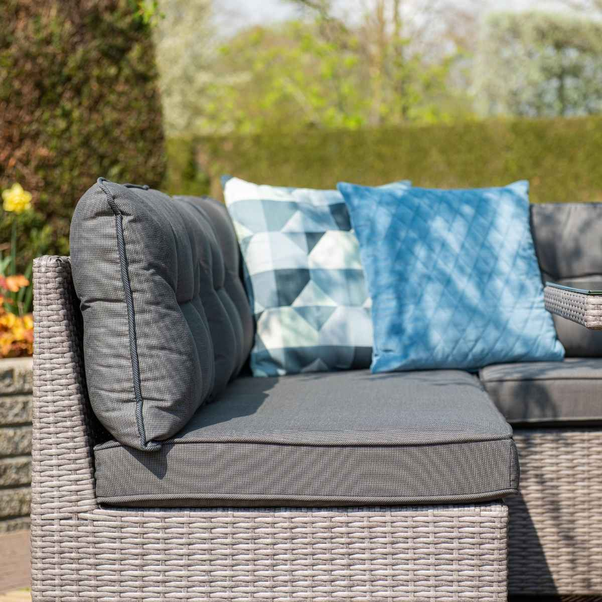 Gros plan sur les coussins et oreillers gris de canapé extérieur. Le canapé est tissé, avec un fond de jardin.