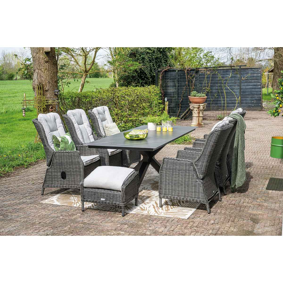 Outdoor dining set with table, chairs, and footrest. Green garden setting.