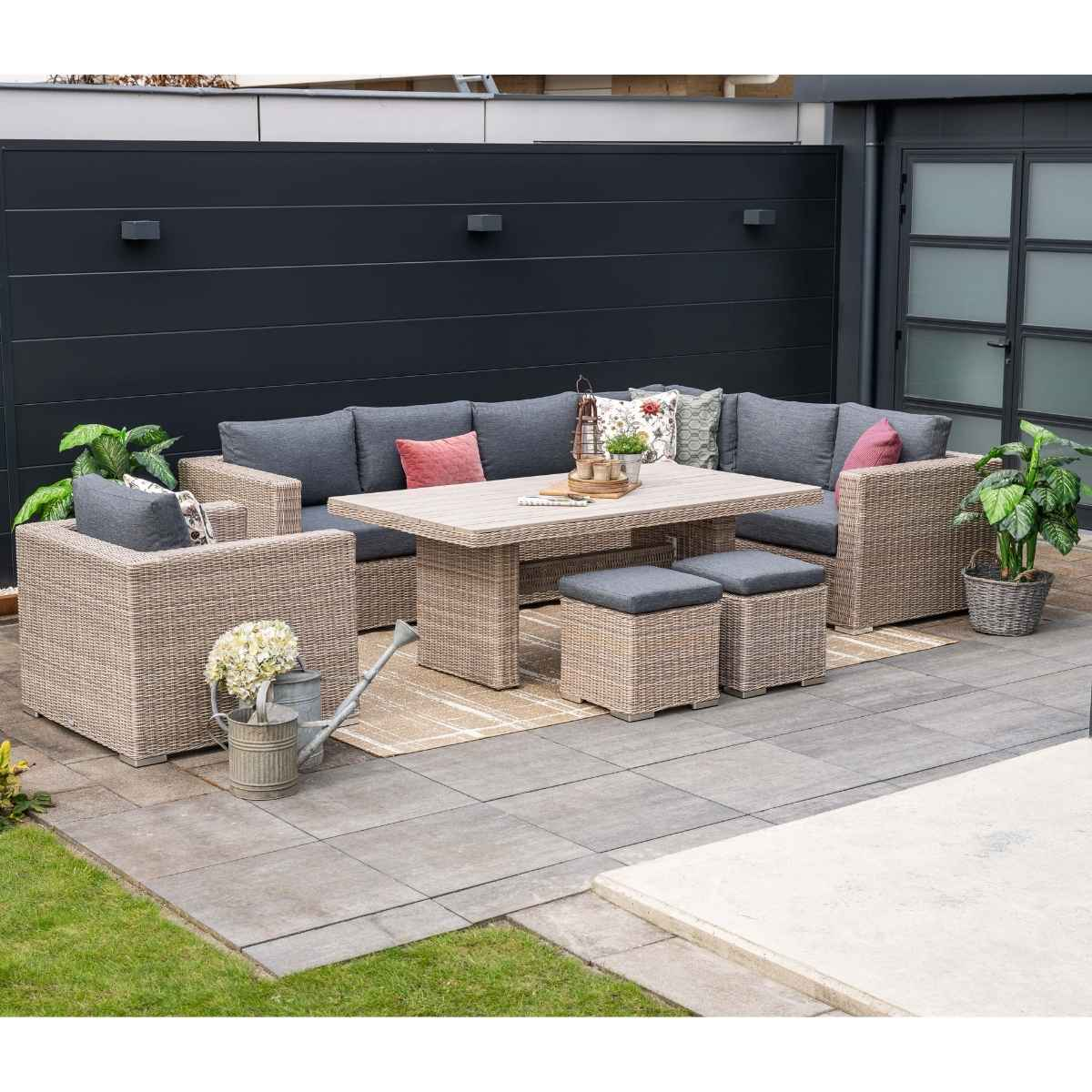 Salon de jardin avec canapé, table, ottomans. Clôture noire en arrière-plan.